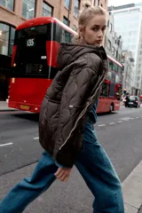 Chaqueta acolchada de color marrón oscuro con diseño de costuras onduladas, cuello subido, capucha ajustable con cordones, cierre frontal con cremallera y cintura ajustable con cordones. Cuenta con bolsillos delanteros de vivo y tejido repelente al agua.