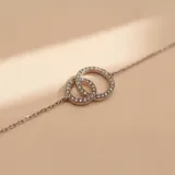 Pulsera de plata 925 con diseño de dos aros entrelazados decorados con circonias brillantes. Cuenta con cadena fina ajustable y cierre de seguridad.