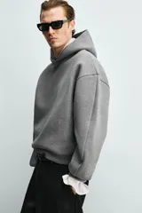 Sudadera tipo hoodie de corte boxy fit, confeccionada en tejido doble y compacto de mezcla de algodón. Presenta cuello con capucha, manga larga y acabados en el mismo tejido.