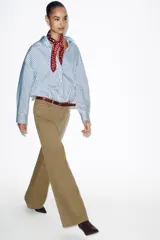 Jeans de tiro alto color azul oscuro, con cinco bolsillos, pernera ancha y nervio marcado en el delantero. Incluye un cinturón fino de cuero sintético marrón con textura de cocodrilo. Cierre frontal con cremallera y botón.