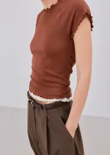 Camiseta ajustada color marrón con mangas cortas y terminaciones con volados delicados en cuello, mangas y dobladillo.