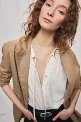 Blazer de silueta amplia y largo por debajo de la cadera, color café, confeccionado en tela suave y liviana. Presenta cuello con solapas, cierre cruzado con botones y bolsillos laterales con tapa.