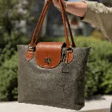 Cartera tote de cuero vacuno color marrón con solapa negra y cierre metálico. Tiene doble asa de mano negra, bolsillo interno con cierre y cierres YKK metálicos.