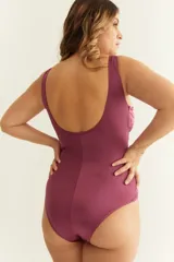 Malla entera color borgoña con escote en V, breteles anchos y aplique metálico dorado en el centro.