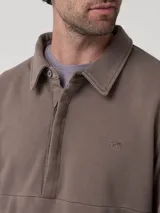 Buzo de hombre con cuello camisero y cierre frontal parcial con tapeta abotonada. Presenta mangas largas y un diseño minimalista con un pequeño logo bordado en el pecho.