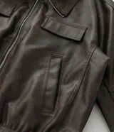 Campera tipo bomber de cuero sintético en color marrón oscuro, con cuello inglés, cierre frontal de cremallera, bolsillos laterales y bolsillos frontales con solapa.