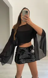 Capa o blusa de gasa negra, con mangas amplias y escote Bardot (hombros descubiertos).