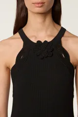 Vestido largo de punto acanalado en color negro, con diseño de sisa americana y cuello redondo decorado con una flor de crochet hecha a mano. Presenta un ribete de trenza de crochet y una abertura lateral en la parte inferior.