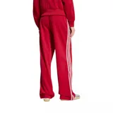 Pantalón deportivo Adidas Firebird Pinstripe de color rojo, con diseño de rayas diplomáticas verticales, corte ancho y pinzas en los laterales. Cuenta con las clásicas tres tiras blancas de la marca en los laterales y el logo del trifolio bordado en la parte frontal. Incluye bolsillos con cierre.