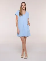 Vestido corto de lino color celeste con cuello camisero, escote en V, mangas cortas, bolsillos laterales invisibles y silueta holgada.
