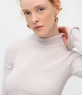 Blusa de chenille color beige, con cuello alto y diseño ajustado al cuerpo. Presenta mangas largas y una textura acanalada en toda la prenda.