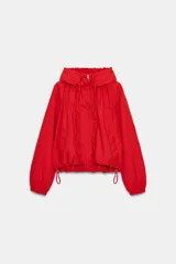 Chaqueta roja de nylon con cuello subido y capucha, manga larga con puños elásticos y cierre frontal con cremallera. Cuenta con bolsillos laterales, detalles de lazadas ajustables en el frente y cordón elástico con stoppers en el bajo.