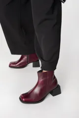Bota corta de cuero color bordó con acabado brillante, diseño de punta cuadrada y taco geométrico de bloque en color negro.