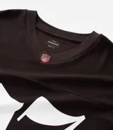 Remera deportiva de algodón color marrón con cuello en V y mangas cortas. Diseño overboxy con estampado de fútbol americano, lettering y rayas contrastantes en blanco.