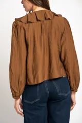 Blusa de color marrón con acabado satinado, cuello en V con volados y lazo de ajuste frontal. Presenta mangas largas con puños elásticos y un corte holgado.
