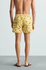 Bañador de hombre de tejido técnico ripstop, color mostaza con estampado floral abstracto en blanco y negro. Presenta cintura elástica ajustable con cordón, bolsillos laterales y bolsillo trasero de plastrón.