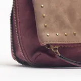 Bandolera de diseño bicolor, combinando una solapa frontal en tono marrón con cuerpo en color bordó. Presenta detalles de tachas metálicas en el borde de la solapa y correa ajustable.