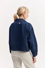 Campera de jean color negro, de calce amplio y largo a la cintura, con cuello alto y cierre frontal con broches a presión.