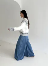 Cardigan de punto con diseño jacquard de inspiración nórdica, en tonos blanco, gris y marrón. Presenta cuello redondo, cierre frontal con botones y mangas largas con puños acanalados.