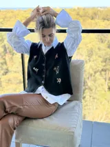 Chaleco negro con cierre frontal de botones, decorado con flores bordadas a mano y costuras decorativas en los bordes.