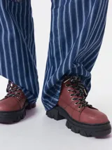 Bota acordonada de estilo montañés con suela track de goma robusta. Confeccionada en cuero con detalles de gamuza en la talonera y tirador trasero. Presenta costuras a contratono y cordones bicolores.