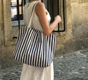 Bolso tote amplio de tela resistente, con diseño de rayas verticales en azul marino y blanco, asas dobles para el hombro y bolsillo frontal.