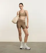 Bermuda deportiva femenina de corte ajustado, color marrón claro con acabado satinado. Presenta pretina ancha y tiro alto.