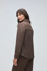 Camisa de lana fina sin teñir, color marrón, con diseño capitoneado y pespuntes decorativos. Presenta cuello clásico, cierre frontal con botones metálicos y dos bolsillos frontales tipo parche.