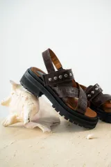 Sandalias de cuero marrón con textura de cocodrilo, diseño de tiras cruzadas con tachas metálicas plateadas y suela track negra de plataforma.