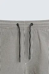 Bañador de hombre color verde claro con finas rayas blancas verticales (efecto seersucker). Tiene cintura elástica ajustable con cordón verde, bolsillos laterales y un bolsillo trasero de vivo.
