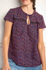 Blusa azul con estampado floral en tonos rosa y celeste, con mangas cortas, cuello redondo con abertura en forma de lágrima y detalle de encaje negro en el pecho.