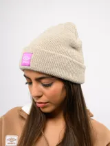 Gorro de lana tipo beanie de tejido acanalado, color beige melange, con vuelta y parche cuadrado en color fucsia con el logo de Umbro.