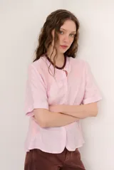 Camisa de lino color rosado, con cuello mao, mangas cortas y cierre frontal con botones. Presenta delicados detalles bordados tono sobre tono en el frente y mangas.