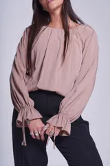 Blusa de manga larga color rosado, con cuello redondo y puños elásticos con volados y lazos decorativos. Presenta un diseño holgado con frunces en el escote.