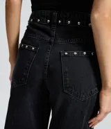 Pantalón wide leg de denim negro con acabado desgastado, tiro medio y aplicación de tachas metálicas a lo largo de los laterales.