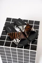 Sandalias chatas con base cuadrada negra y tiras cruzadas de cuero con estampado animal print de cebra y tigre.