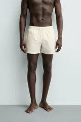 Short de baño de color beige con textura seersucker, cintura elástica con cordón ajustable, bolsillos laterales y forro interior.