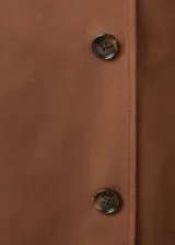 Chaqueta larga tipo trench color marrón, con diseño recto, solapas anchas, doble botonadura, bolsillos laterales y cinturón desmontable de la misma tela.
