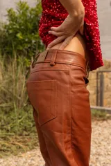 Pantalón de cuero color marrón con estampado abstracto, corte acampanado y abertura en el ruedo.