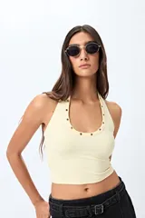 Top halter color marrón, con escote redondeado y detalle de ojales metálicos a lo largo del cuello. Presenta un diseño ajustado al cuerpo y espalda descubierta.
