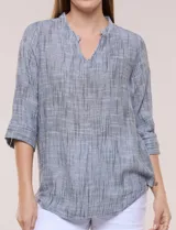 Blusa de silueta relajada con textura tramada, color azul con rayas verticales en tonos rosados, celestes y amarillos. Cuenta con cuello mao abierto en V y mangas tres cuartos amplias con pequeña abertura lateral en el puño.