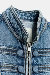Chaqueta denim entallada de cuello redondo y manga larga, con cierre frontal de cremallera metálica. Presenta detalles de aplicaciones en el mismo tejido y pasamanería frontal de inspiración militar.