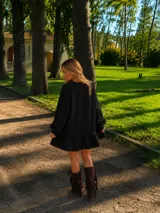 Vestido corto de lino color negro, con silueta amplia y relajada, mangas largas abullonadas y detalle de volado en el ruedo.