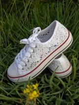 Zapatillas bajas de lona blanca con detalles de encaje bordado y suela de goma con líneas rojas y negras.