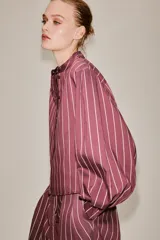 Camisa de cuello subido y manga larga con puños anchos, confeccionada en tejido satinado con diseño de rayas verticales.