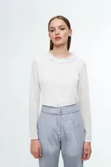Remera de manga larga confeccionada en tul elastizado con cristales brillantes aplicados. Presenta un corte entallado, escote a la base con detalle de volado y forro a tono en la parte delantera.