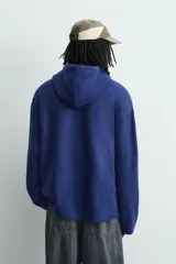Chaqueta de punto de corte relajado, color azul, con capucha, cierre frontal con cremallera y acabados en rib en puños y bajo.