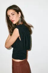 Top negro de punto con cuello redondo y manga corta estilo sisa. Presenta un diseño holgado en la parte superior con delicados frunces y detalle drapeado, y una sección inferior ajustada con frunces verticales y horizontales.