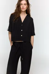 Camisa de cuello solapa y escote pico, color verde militar, con manga corta con trabilla y botón, y cierre frontal con botones.