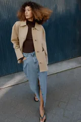 Chaqueta de corte recto y estilo camisero en color beige, con cuello solapa, manga larga y cierre frontal con botones. Presenta dos bolsillos delanteros de plastrón.